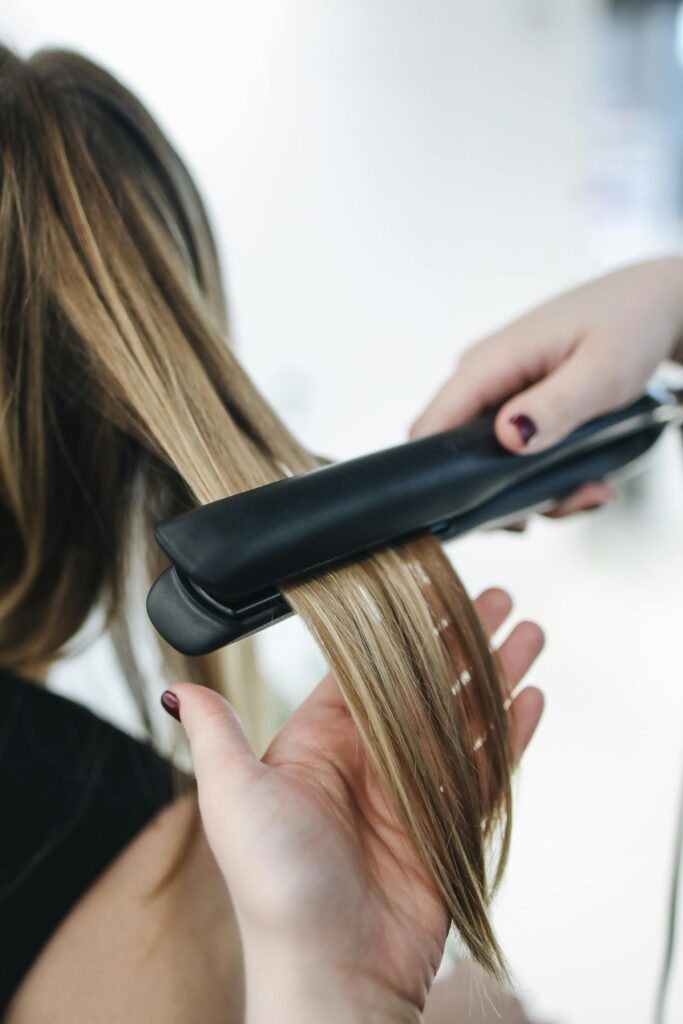 Close-up of a hairstylist using a flat iron on blonde hair in a salon setting.